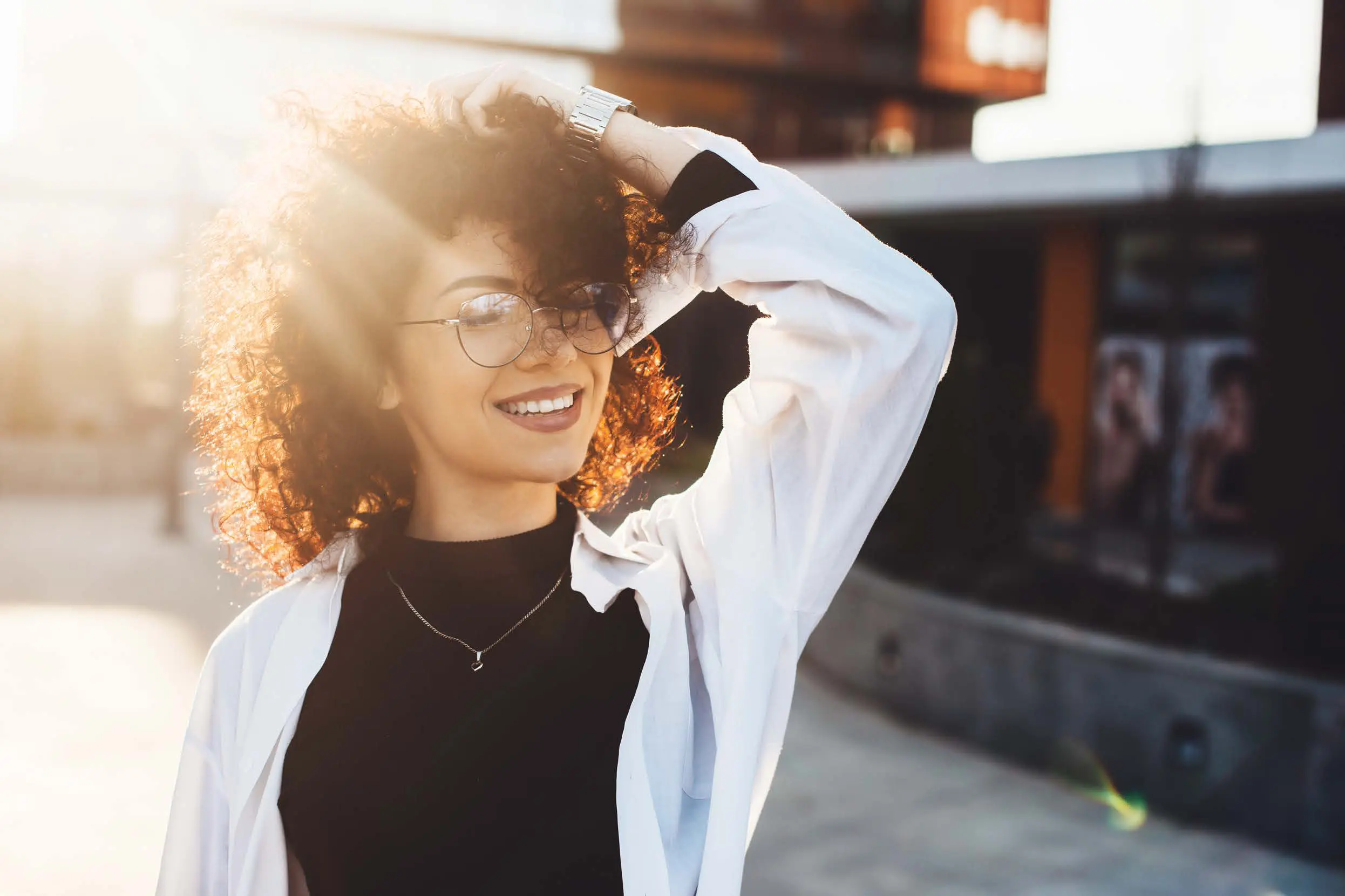 A woman with curly hair and glasses is smiling.